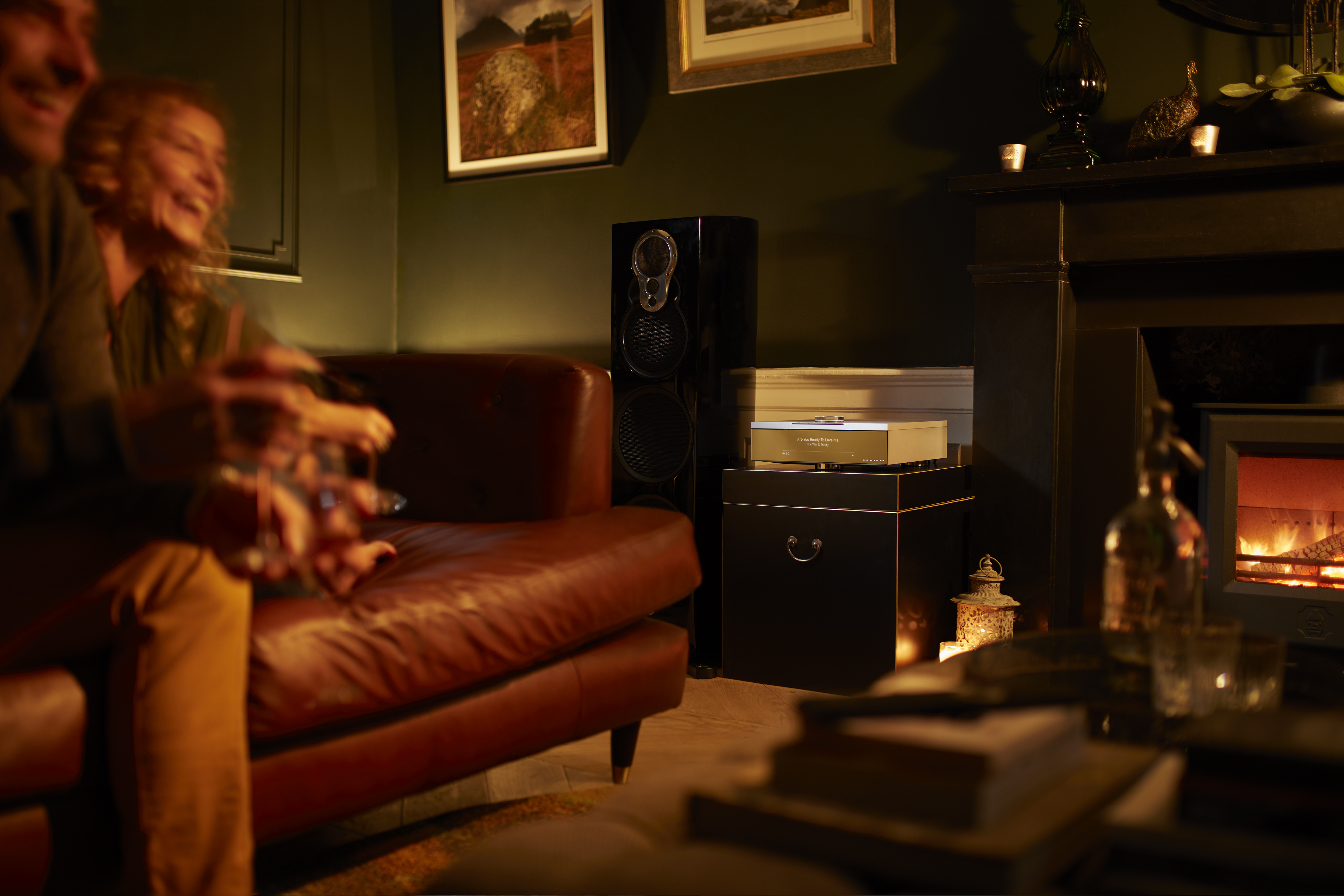 A Linn Klimax DSM network music player and Linn loudspeaker in a warmly lit living room by firelight in the evening.