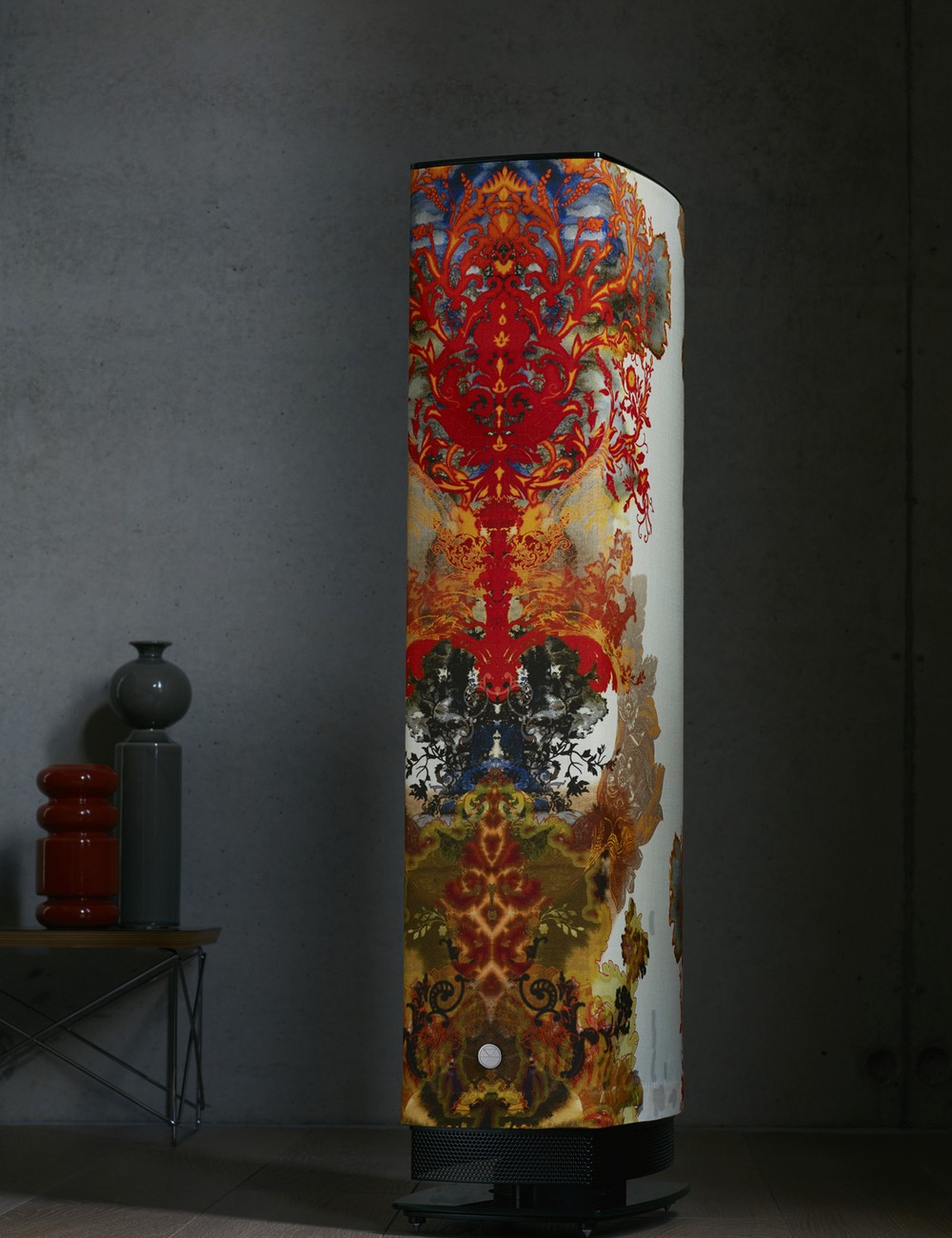 A Linn 530 loudspeaker finished in bespoke Grand Blotch Damask fabrik, lit against a dark concrete wall.