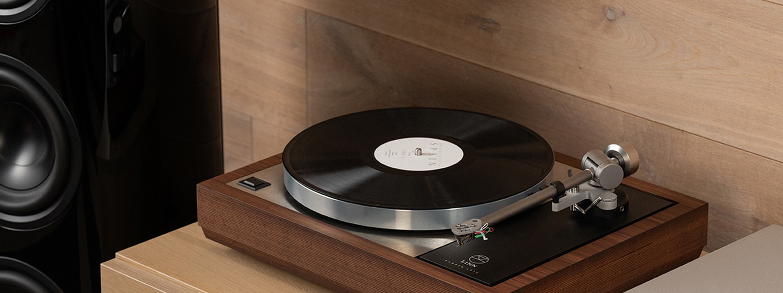 A Linn Klimax LP12 turntable playing a record, beside black Linn 360 loudspeakers in a warm walnut-panelled room.
